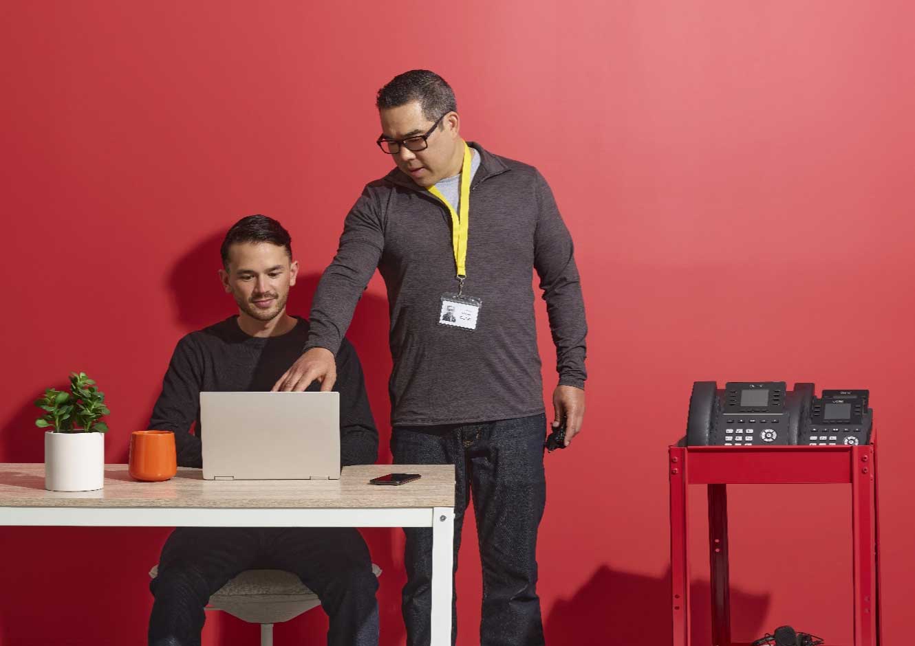 Easy Deployment and Unparalleled support image - A man working on his workstation, another one standing to help support pointing to the screen