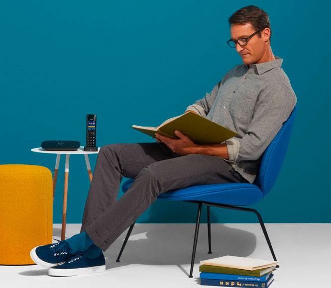 Ooma Home Phone Service Hero Image - A man sitting down with Telo Home Phone on a table next to him